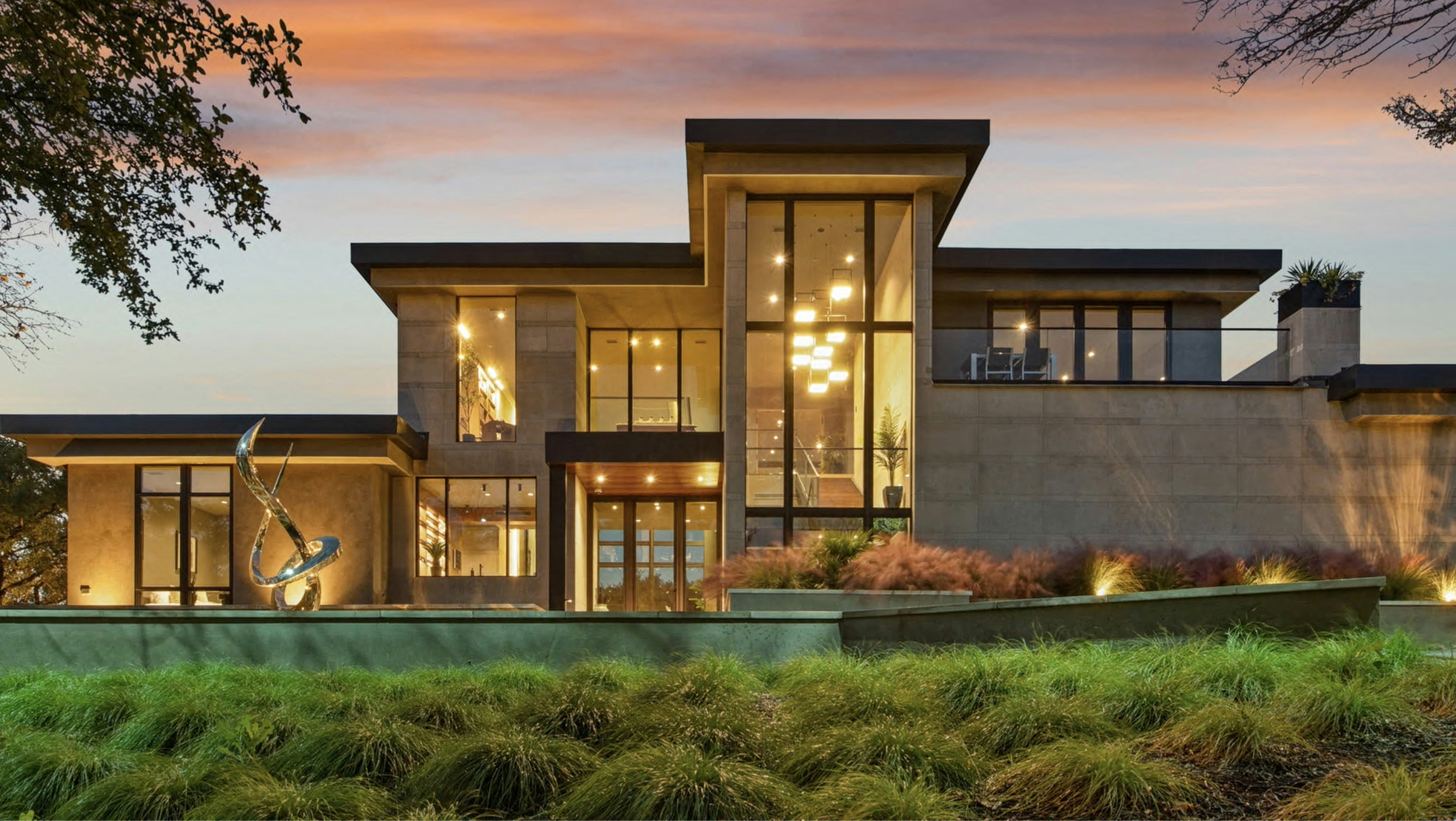 A modern luxury home at dusk, glass walls lit from inside